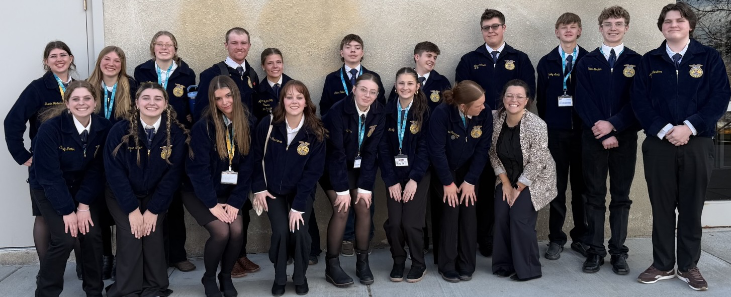 A group of students wearing blue jackets pose together outdoors for a group photo.